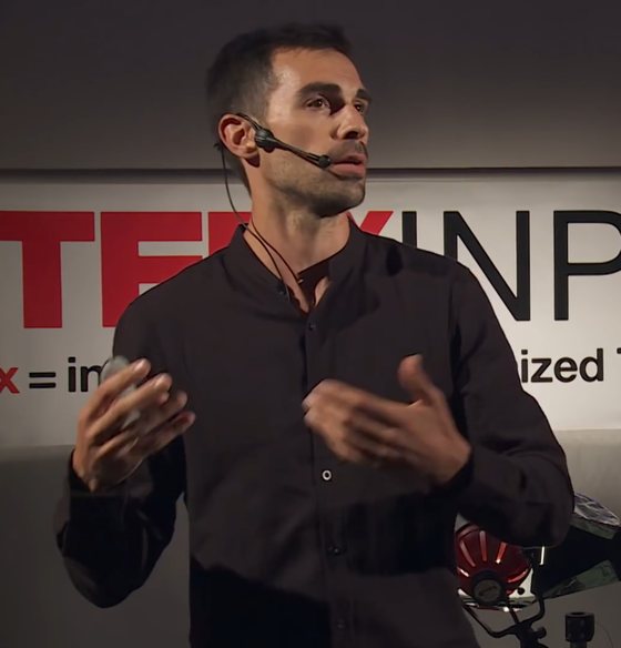 Dimitri Garcia sur la scène d'une conférence TEDx, micro-casque, devant le kakémono TEDxINPENSAT